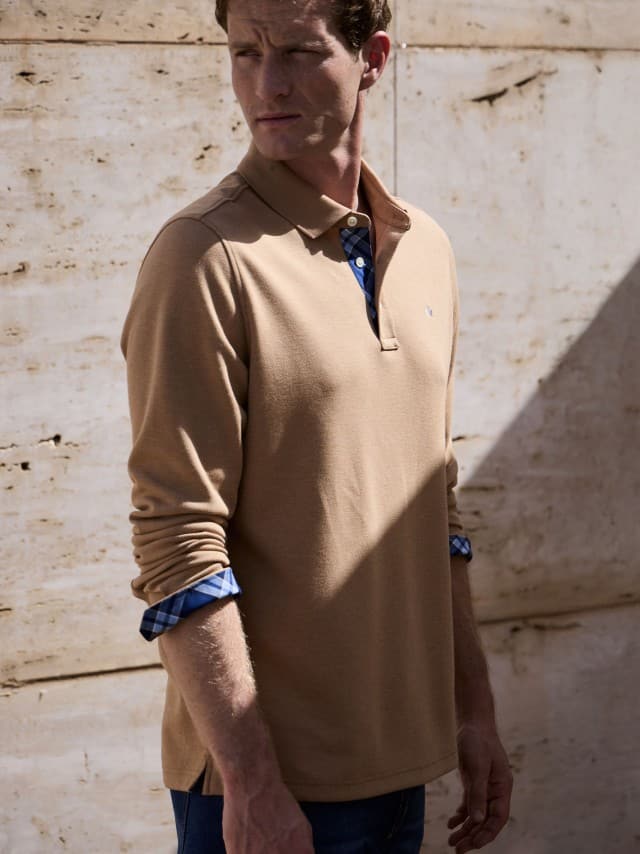 Ein Mann vor einer Natursteinwand trägt ein Premium Polo in der Farbe Latte, dazu eine Jeans. Ein Mann vor einer Natursteinwand trägt ein Premium Polo in der Farbe Latte, dazu eine Jeans.