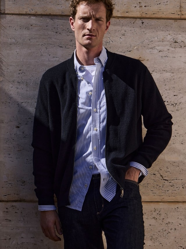 Ein Mann vor einer Natursteinwand trägt die Zip-Jacke Ministruktur in Marine, darunter ein hellblaues Hemd und dazu eine Jeans. Ein Mann vor einer Natursteinwand trägt die Zip-Jacke Ministruktur in Marine, darunter ein hellblaues Hemd und dazu eine Jeans.