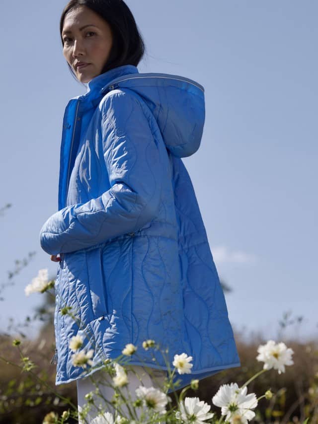 Eine Frau steht im Freien und trägt eine hellblaue gesteppte Jacke mit Kapuze.