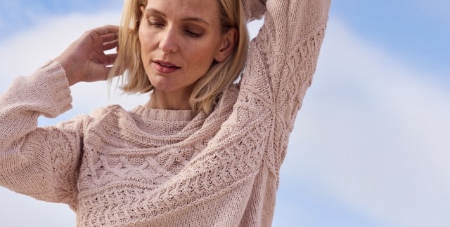 Eine Frau trägt einen hellrosa, grob gestrickten Pullover mit strukturiertem Muster. Der Stil wirkt gemütlich und lässig, passend für kühles Wetter. Eine Frau trägt einen hellrosa, grob gestrickten Pullover mit strukturiertem Muster. Der Stil wirkt gemütlich und lässig, passend für kühles Wetter.