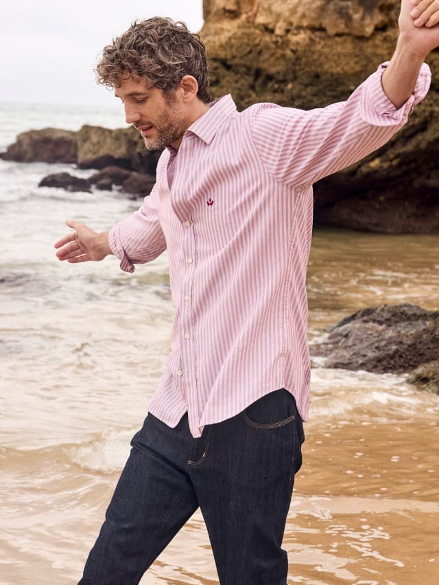 Ein Mann an der Küste trägt ein rot gestreiftes Hemd, dazu eine Charakter-Jeans. Ein Mann an der Küste trägt ein rot gestreiftes Hemd, dazu eine Charakter-Jeans.