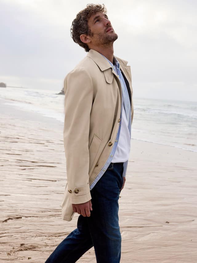 Ein Mann am Strand trägt einen Baumwoll Mantel in Beige, darunter ein Hemd und dazu eine Charakter-Jeans. Ein Mann am Strand trägt einen Baumwoll Mantel in Beige, darunter ein Hemd und dazu eine Charakter-Jeans.