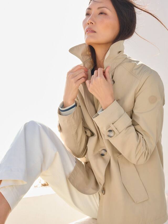 Eine Frau trägt einen hellen Trenchcoat zu einer weißen Hose, was clean, zeitlos und ruhig‑elegant wirkt. Eine Frau trägt einen hellen Trenchcoat zu einer weißen Hose, was clean, zeitlos und ruhig‑elegant wirkt.