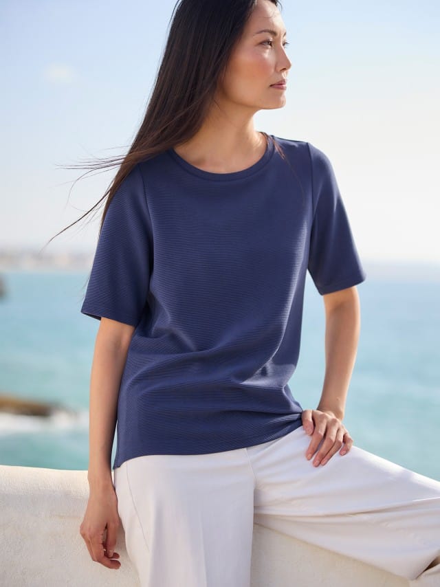 Eine Frau trägt ein dunkelblaues T‑Shirt zu einer weißen Hose, was ruhig, klar und sommerlich entspannt wirkt. Eine Frau trägt ein dunkelblaues T‑Shirt zu einer weißen Hose, was ruhig, klar und sommerlich entspannt wirkt.