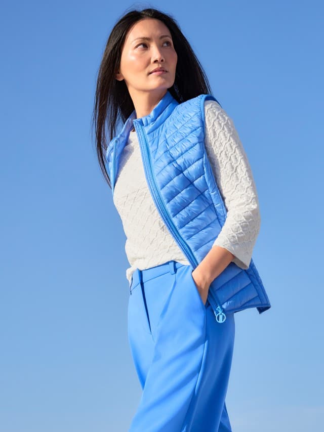 Eine Frau trägt eine hellblaue Steppweste zu einem strukturierten hellen Oberteil und blauen Hosen, was frisch, modern und aktiv‑leicht wirkt. Eine Frau trägt eine hellblaue Steppweste zu einem strukturierten hellen Oberteil und blauen Hosen, was frisch, modern und aktiv‑leicht wirkt.