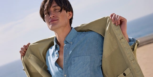 Ein Mann trägt ein blaues Hemd, darüber eine offene leichte Jacke in Khaki.