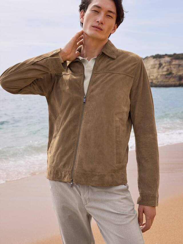 Ein Mann trägt eine hellbraune Veloursjacke zu einem hellen Shirt und grauen Hosen, was hochwertig, natürlich und ruhig‑entspannt wirkt.