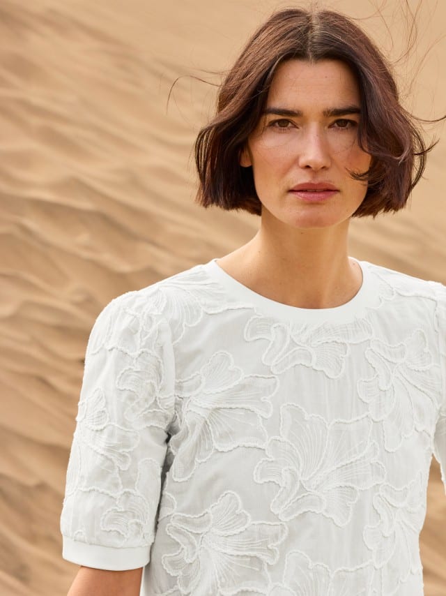 Eine Frau steht in den Dünen und trägt ein weißen Shirt mit Stickerei. Eine Frau steht in den Dünen und trägt ein weißen Shirt mit Stickerei.