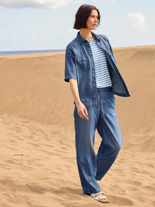 Eine Frau steht in den Dünen und trägt ein Outfit aus Denim mit einem gestreiften Shirt. Eine Frau steht in den Dünen und trägt ein Outfit aus Denim mit einem gestreiften Shirt.
