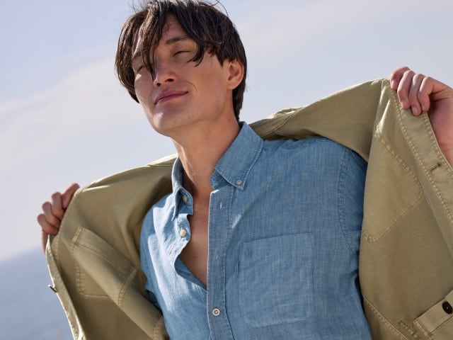 Ein Mann trägt ein blaues Hemd, darüber eine offene leichte Jacke in Khaki.