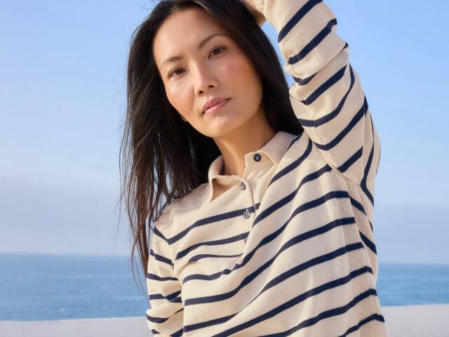 Eine Frau am Meer, trägt einen gestreiften Polo-Pullover.