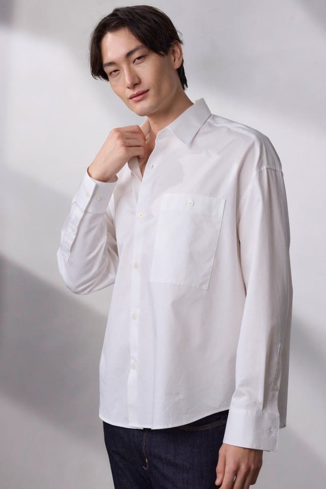 Ein Mann trägt ein weißes Hemd und steht vor einem schlichten, hellen Hintergrund.