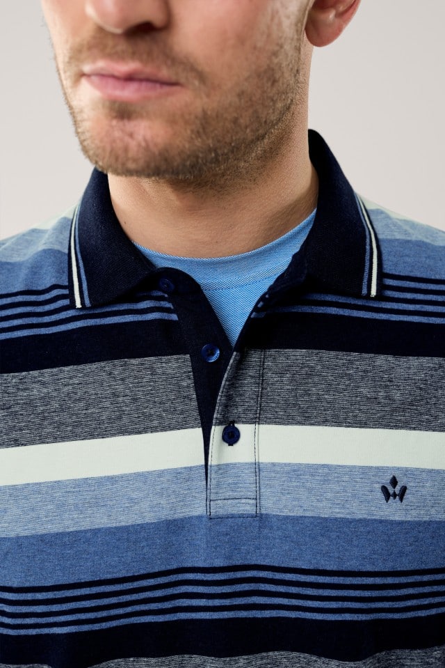 Ein Mann trägt ein langärmliges Poloshirt mit breiten Querstreifen in verschiedenen Blau-, Grau- und Weißtönen; der dunkle Kragen hat feine helle Streifendetails und unter dem Shirt ist ein hellblaues T-Shirt zu sehen.