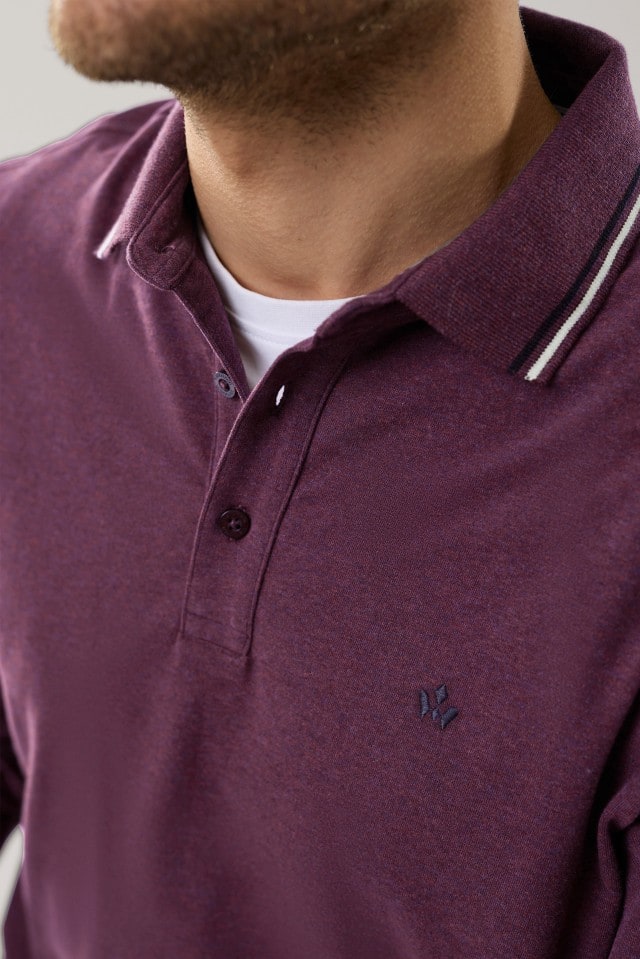Ein Mann trägt ein weinrotes Poloshirt mit feiner, heller Streifenverzierung am Kragen und dezenter Stickerei auf der Brust; darunter blitzt ein weißes T-Shirt leicht hervor.