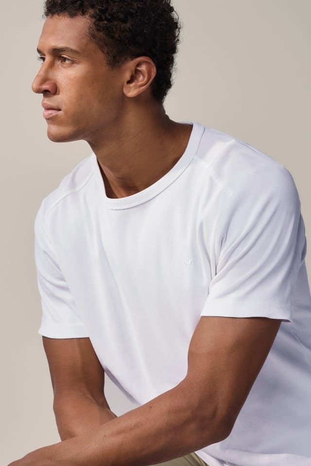 Nahaufnahme eines Mannes mit lockigem Haar im weißen T-Shirt, der seitlich nach links blickt.