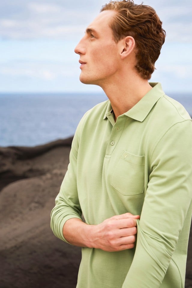 Ein Mann trägt ein hellgrünes Langarm‑Poloshirt und blickt seitlich in die Ferne.