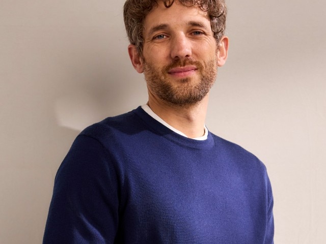 Ein Mann trägt einen blauen Pullover mit Rundhals-Ausschnitt. 