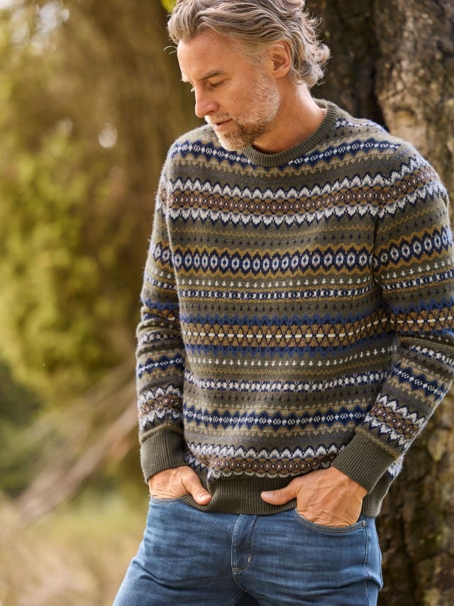Ein Mann trägt einen Fair-Isle-Pullover und steckt die Hände in die Taschen einer blauen Jeans.