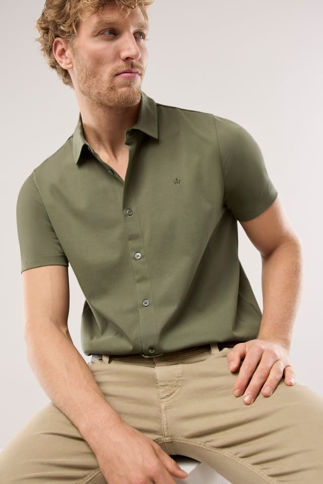 Ein Mann trägt ein Shirtpolo in Khaki, dazu eine Jeans in Beige.
