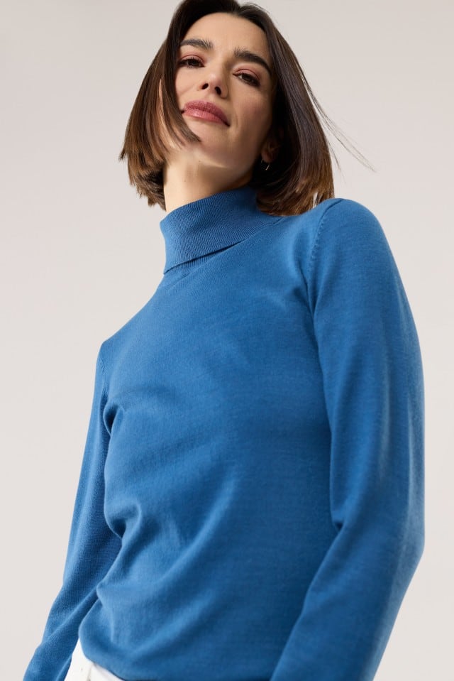 Eine Frau trägt einen blauen Rollkragenpullover aus feinem Strick. Der Look ist schlicht, elegant und ideal für kühle Tage.