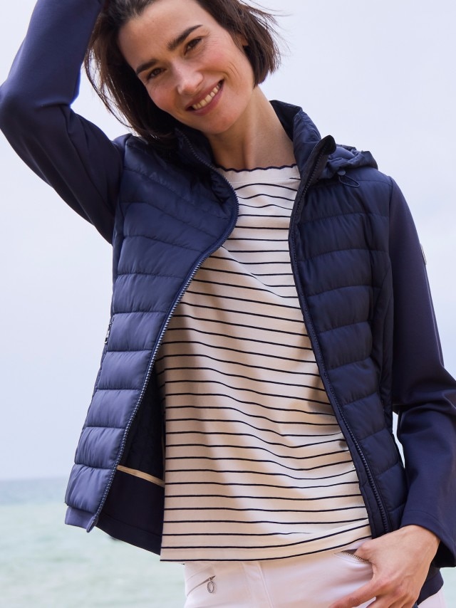 Ein Frau trägt die Steppjacke Materialmix in Marine, darunter ein gestreiftes Shirt und dazu eine weiße Hose. 
