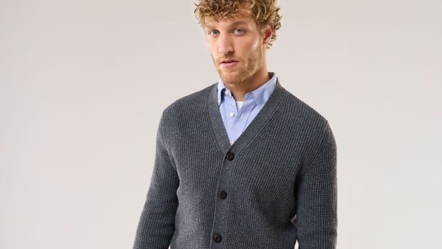 Ein Mann trägt einen Cardigan in Grau und darunter ein hellblaues Hemd.