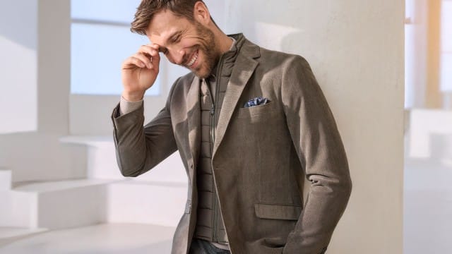 Ein Mann trägt ein Mikrovelours Sakko 2 in 1 in Beige, dazu eine karierte Gürtel-Chino Wool-Look.