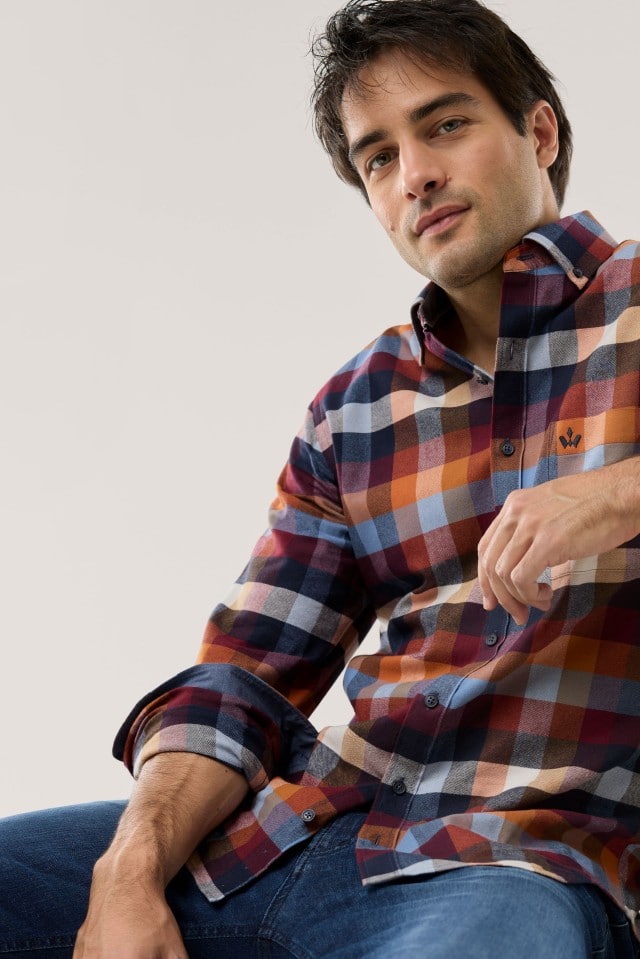 Eine Person trägt ein kariertes Hemd in warmen Rot-, Blau- und Orangetönen, kombiniert mit einer Jeans für einen lässig-modernen Look.