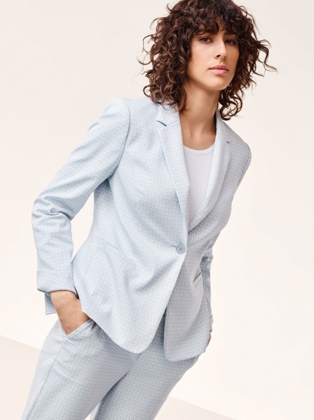 Frau in Rauchblau/Weißem Jacquardblazer mit passender Hose.