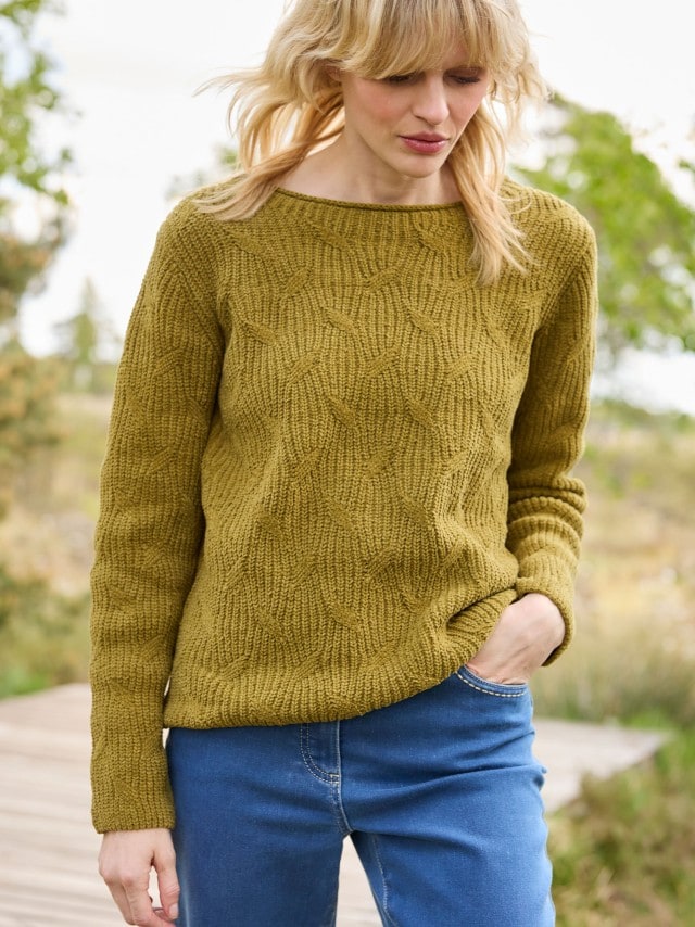 Eine Frau trägt einen Baumwoll-Samt Pullover in Zederngrün, dazu eine Jeans.