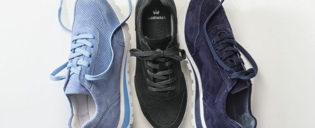 Drei sportliche Schnürschuhe aus Veloursleder in Hellblau, Schwarz und Dunkelblau liegen nebeneinander auf weißem Hintergrund. Die Schuhe wirken bequem und modern, ideal für einen lässigen Alltagslook.