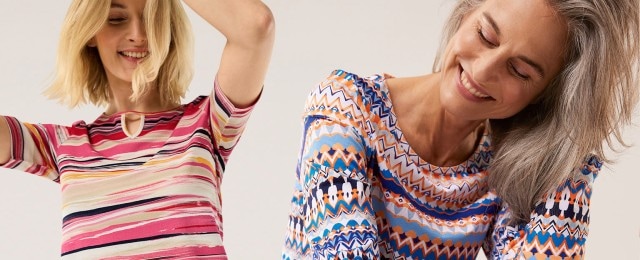Zwei Frauen tragen farbenfrohe Oberteile mit auffälligen Mustern: Eine mit einem kurzärmeligen Shirt in rosafarbenen Streifen, die andere mit einem langärmeligen Shirt im bunten Zickzack-Design. Die Looks strahlen Lebensfreude aus und eignen sich ideal für einen frischen, modernen Stil.