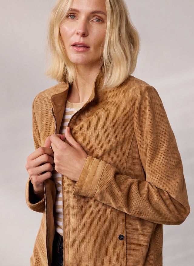 Frau trägt eine hellbraune Wildlederjacke mit feiner Lochstruktur und darunter ein gestreiftes Oberteil. Der Look wirkt lässig und elegant zugleich.