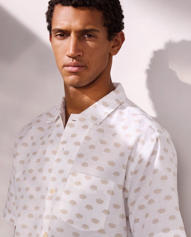 Ein Mann vor einem hellen Hintergrund, trägt ein weißes Hemd mit Muster.