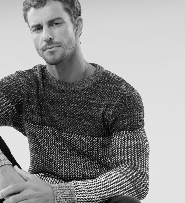 Ein Mann trägt einen Pullover mit aufwendiger Strickstruktur und raffiniertem Farbverlauf.