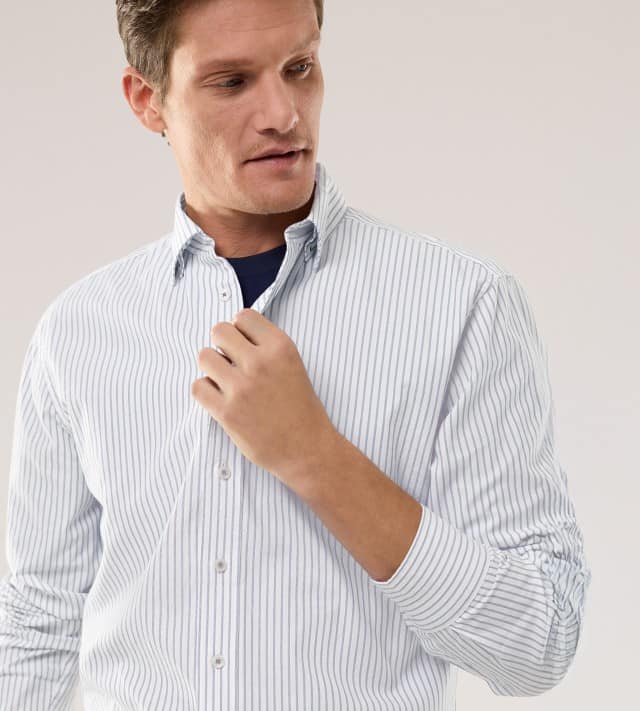 Ein Mann trägt ein weißes Hemd mit Streifen, darunter ein Shirt in Marineblau.