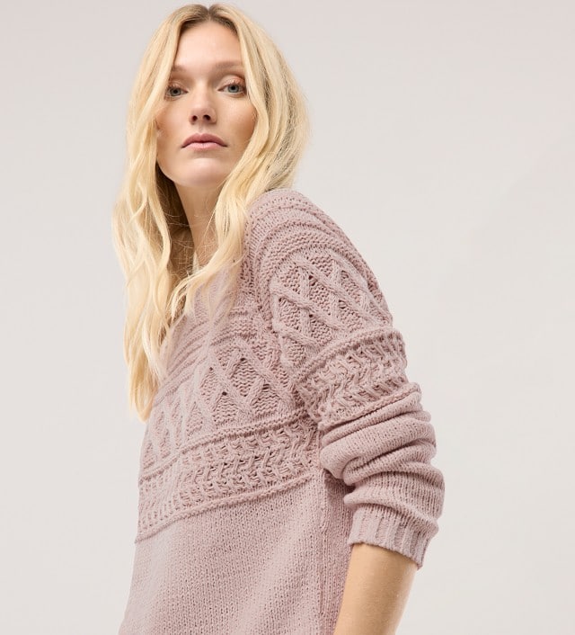 Eine Frau vor einem hellen Hintergrund trägt einen Pullover aus softem Bändchengarn in Altrosa.