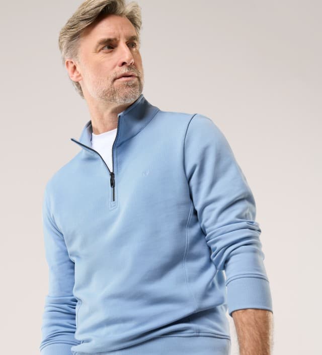 Ein Mann vor einem hellen Hintergrund trägt einen Essential Troyer in Chambray. 