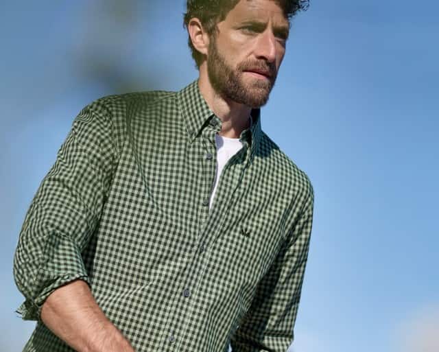 Ein Mann trägt ein kariertes Hemd, darunter ein weißes Shirt.