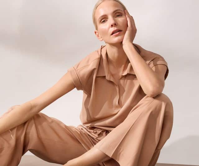 Ein Frau sitzt lässig auf dem Boden und trägt ein Poloshirt Edelmodal in der Farbe Praline, dazu eine passende Hose.