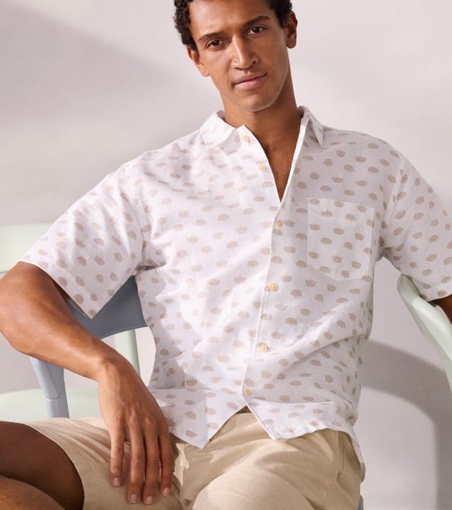 Ein Mann sitzt lässig auf eine Stuhl und trägt ein weißes Hemd mit Muster, dazu eine helle Hose. Ein Mann sitzt lässig auf eine Stuhl und trägt ein weißes Hemd mit Muster, dazu eine helle Hose.