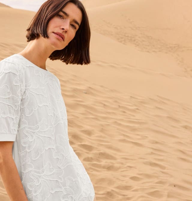 Eine Frau steht in den Dünen und trägt ein weißes Shirt.