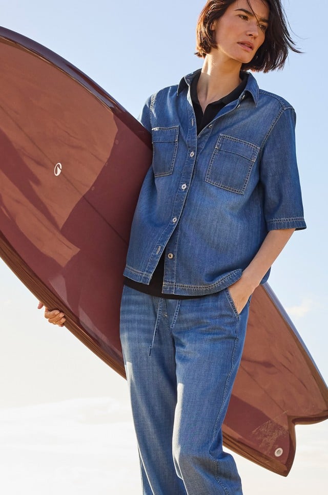 Person trägt ein legeres Denim-Outfit aus Jeanshemd und Jeanshose im Freizeitstil.