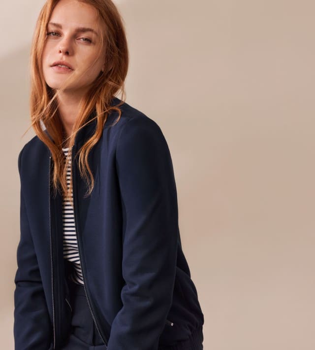 Eine Frau trägt ein dunkelblaues, glattes Jackenoberteil über einem schwarz-weiß gestreiften Shirt mit Rundhalsausschnitt.