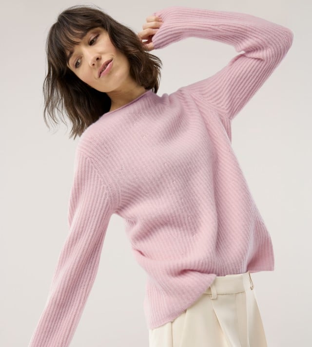Eine Frau schaut nach unter zur Seite und trägt einen Cashmere Pullover in Puder, dazu eine helle Hose.