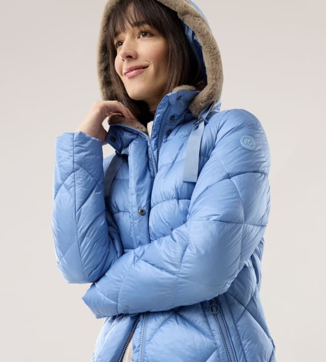 Ein Frau schaut lächelnd zur Seite und trägt eine Steppjacke mit Kuschelkragen und Kapuze in der Farbe Ozeanblau.