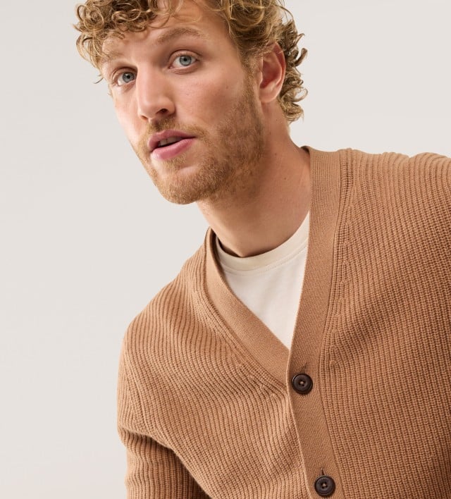 Ein Mann trägt einen Patentstrick-Cardigan in der Farbe Karamell, darunter ein weißes Shirt.