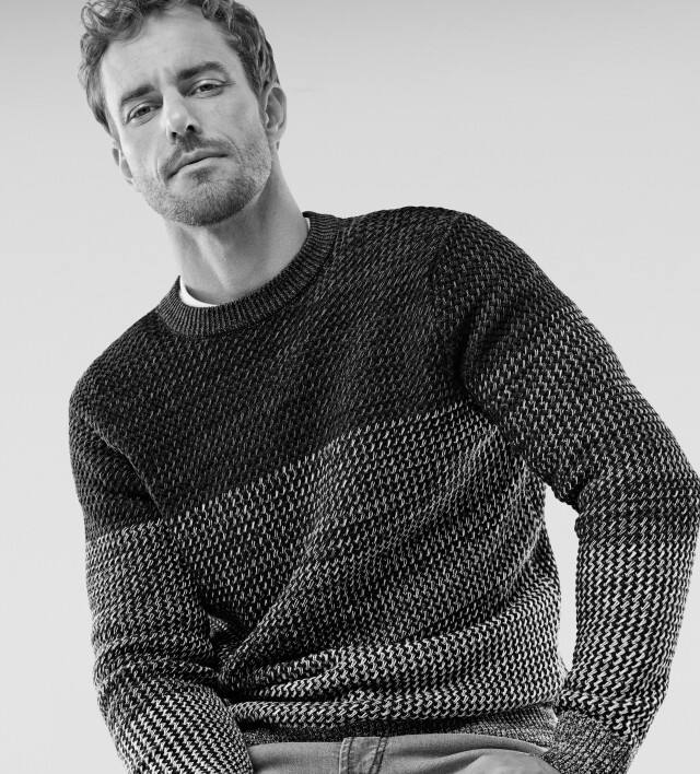 Ein Mann trägt einen Pullover mit aufwendiger Strickstruktur und raffiniertem Farbverlauf.