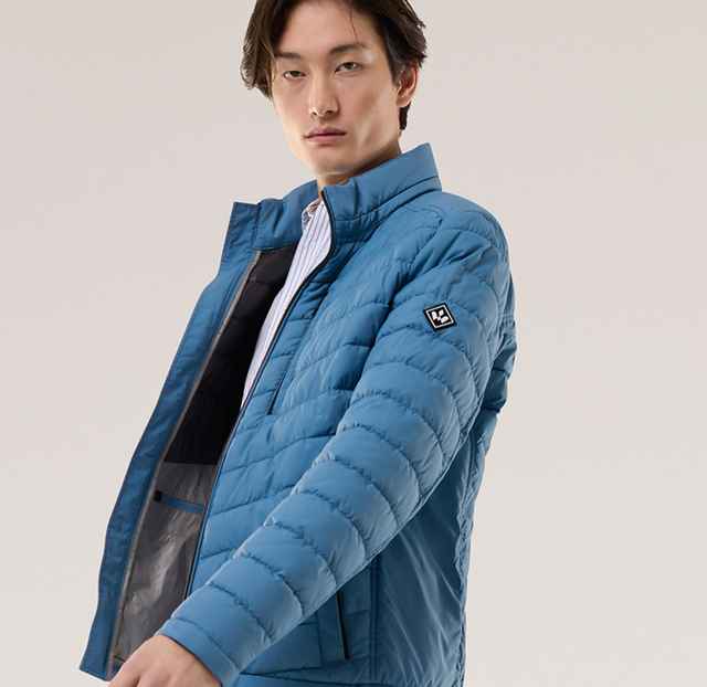 Ein Mann trägt eine gesteppte Jacke in Blau, darunter ein gestreiftes Hemd.