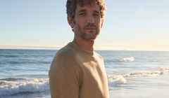 Ein Mann am Strand, trägt einen Pullover in Beige.